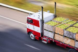Caminhão transportando legumes na estrada ilustra logística no agronegócio.